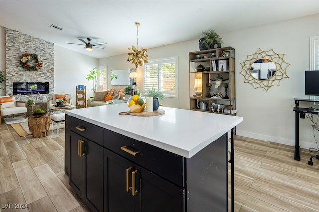 kitchen with light hardwood / wood-style floors, a kitchen island, ceiling fan, and a stone fireplace