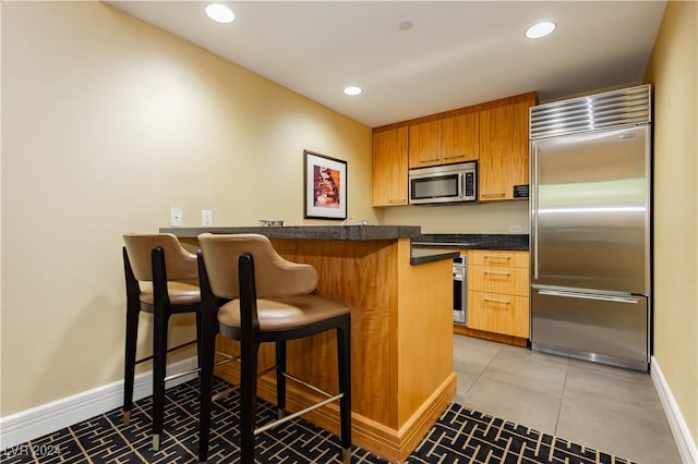 kitchen with tile patterned flooring, kitchen peninsula, stainless steel appliances, and a breakfast bar