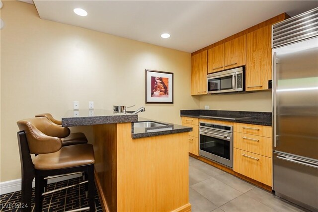 kitchen with a kitchen bar, stainless steel appliances, sink, kitchen peninsula, and light tile patterned flooring