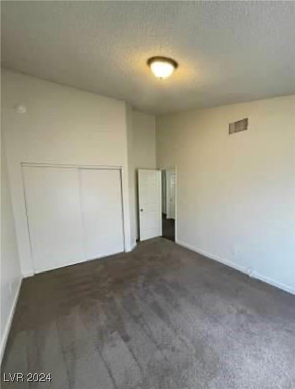 unfurnished bedroom with a textured ceiling, dark colored carpet, and a closet