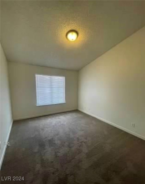 empty room featuring a textured ceiling, dark carpet, and lofted ceiling