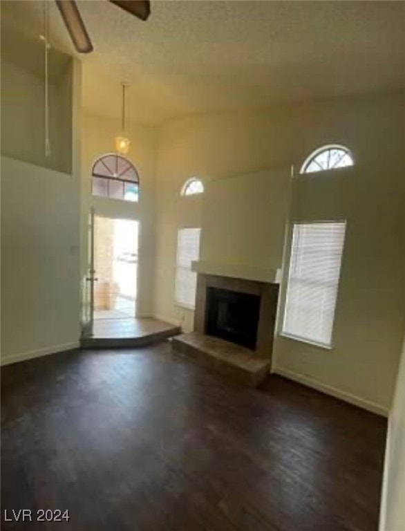 unfurnished living room with a textured ceiling, a healthy amount of sunlight, ceiling fan, and dark wood-type flooring