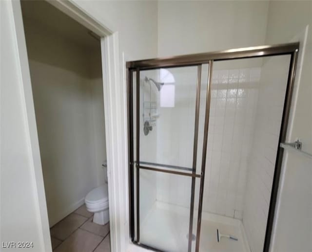 bathroom featuring tile patterned flooring, a shower with shower door, and toilet