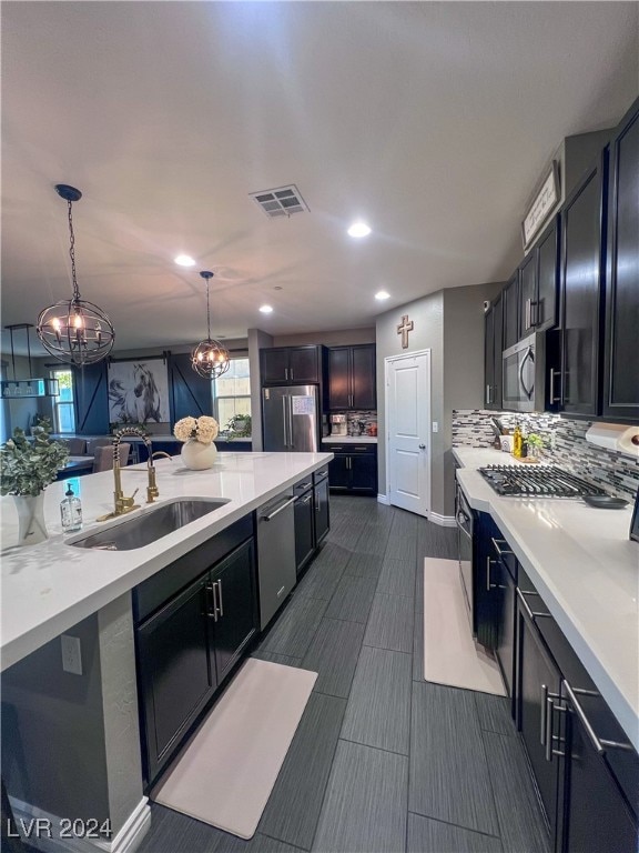 kitchen with pendant lighting, stainless steel appliances, sink, decorative backsplash, and a chandelier