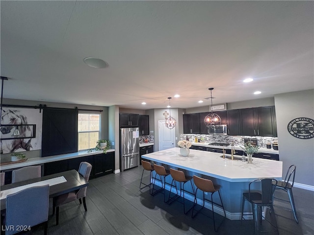 kitchen with a barn door, stainless steel appliances, sink, an island with sink, and dark wood-type flooring