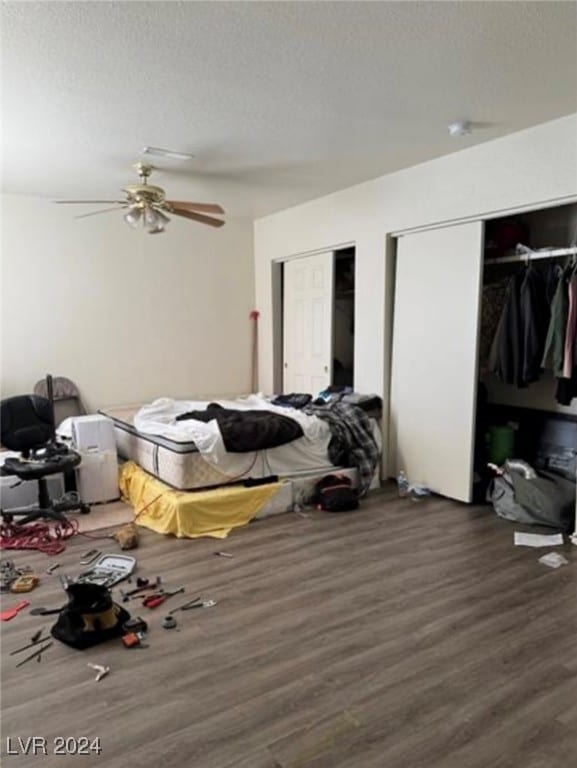 bedroom featuring a textured ceiling, ceiling fan, dark hardwood / wood-style floors, and multiple closets