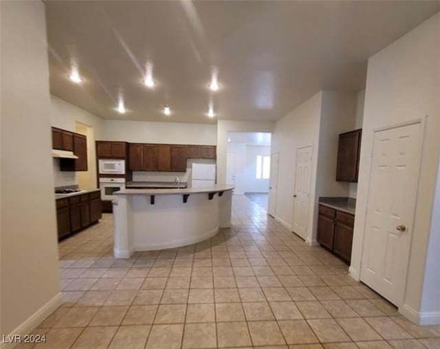 kitchen with white appliances, dark brown cabinets, a kitchen bar, and light tile patterned flooring