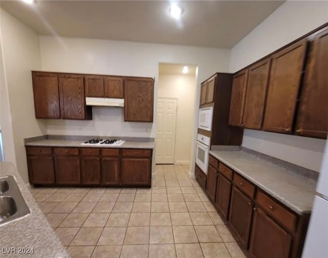 kitchen featuring light tile patterned floors, dark brown cabinetry, and white appliances