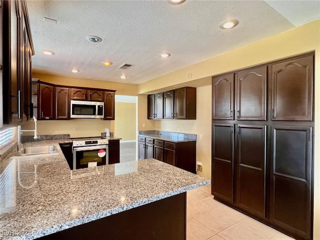 kitchen featuring stainless steel appliances, dark brown cabinets, light stone counters, and kitchen peninsula