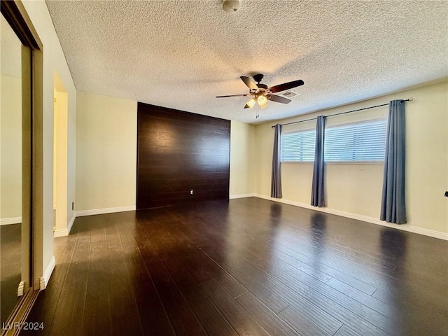 spare room featuring dark wood-type flooring, ceiling fan, wooden walls, and a textured ceiling