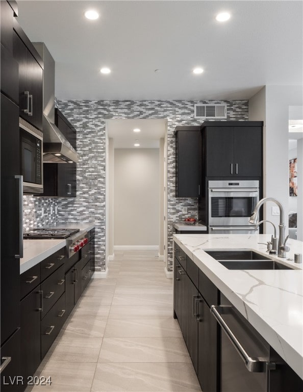 kitchen with stainless steel appliances, sink, light stone countertops, wall chimney exhaust hood, and decorative backsplash