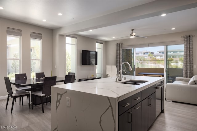 kitchen featuring a center island with sink, light stone countertops, sink, ceiling fan, and light hardwood / wood-style flooring