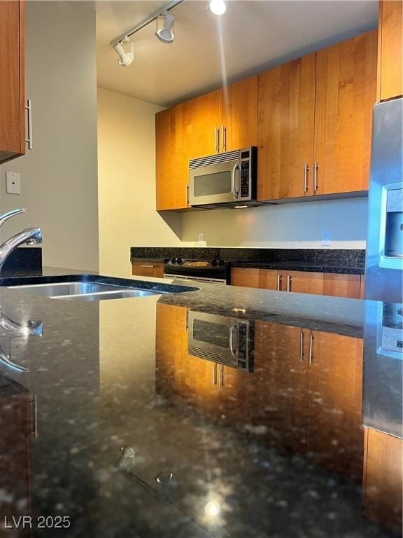 kitchen featuring track lighting, appliances with stainless steel finishes, sink, and dark stone countertops