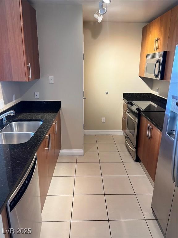 kitchen with dark stone countertops, sink, light tile patterned floors, and appliances with stainless steel finishes