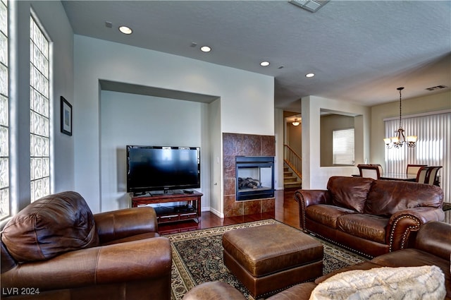 living room featuring a tile fireplace, hardwood / wood-style flooring, an inviting chandelier, and a textured ceiling