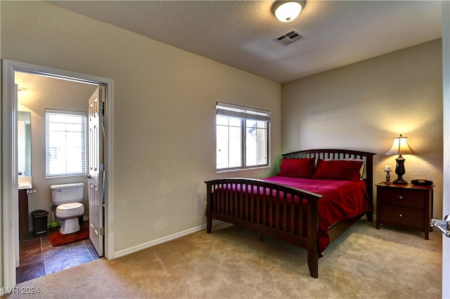 carpeted bedroom featuring ensuite bath and multiple windows