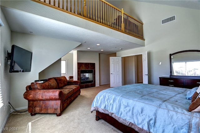 carpeted bedroom featuring a tile fireplace and a towering ceiling