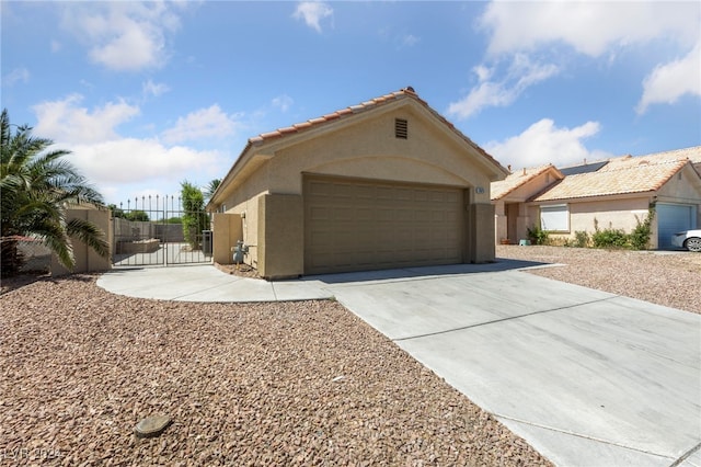 view of front of home with a tile roof, stucco siding, an attached garage, a gate, and driveway