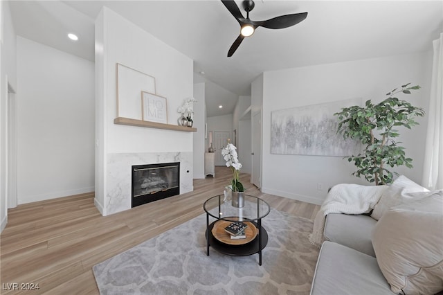 living room featuring light hardwood / wood-style floors, vaulted ceiling, ceiling fan, and a fireplace