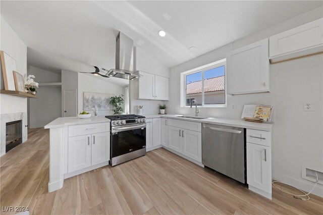 kitchen with a premium fireplace, appliances with stainless steel finishes, island range hood, sink, and white cabinets