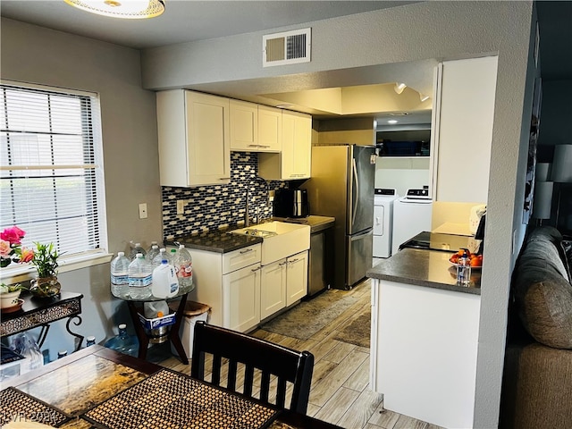 kitchen featuring backsplash, washer and dryer, stainless steel refrigerator, sink, and light wood-type flooring