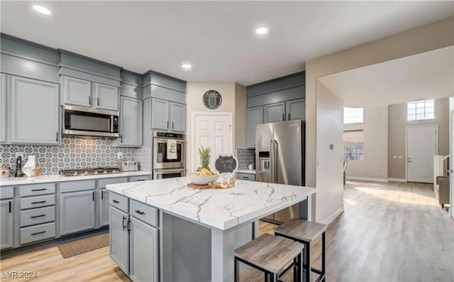 kitchen featuring a center island with sink, light stone counters, stainless steel appliances, and tasteful backsplash