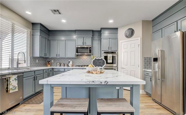 kitchen featuring light stone countertops, decorative backsplash, stainless steel appliances, light hardwood / wood-style floors, and a kitchen island