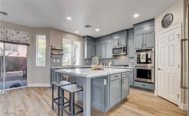 kitchen featuring backsplash, a kitchen island, light wood-type flooring, and appliances with stainless steel finishes