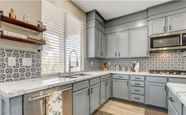 kitchen featuring decorative backsplash, light stone countertops, stainless steel appliances, sink, and light hardwood / wood-style floors