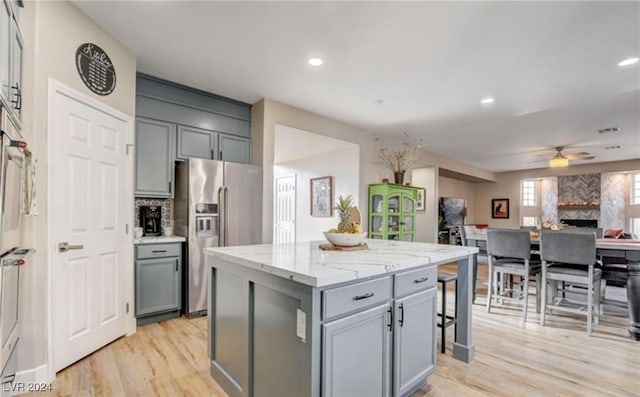 kitchen featuring ceiling fan, a center island, light stone counters, light hardwood / wood-style flooring, and stainless steel fridge