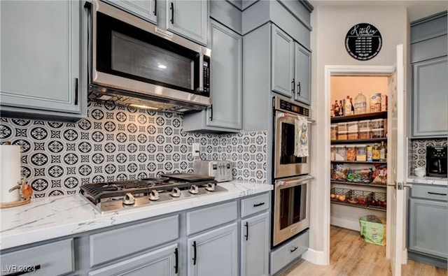 kitchen with light stone countertops, light wood-type flooring, stainless steel appliances, and gray cabinets