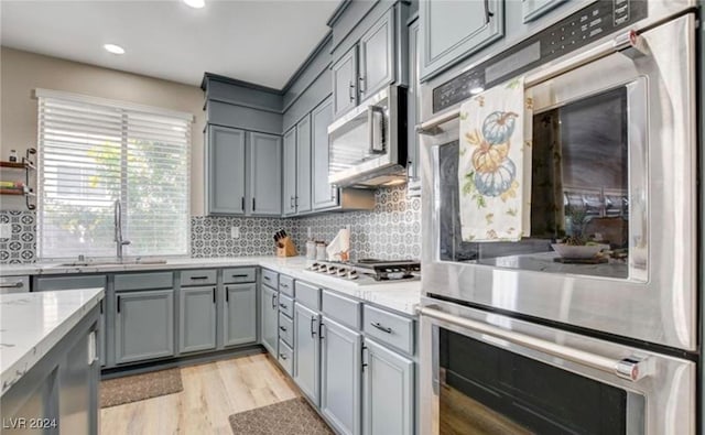 kitchen with sink, light stone countertops, light wood-type flooring, appliances with stainless steel finishes, and tasteful backsplash