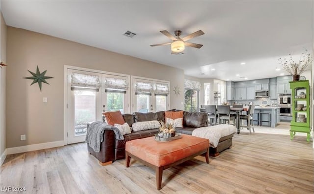 living room with french doors, light hardwood / wood-style floors, ceiling fan, and a healthy amount of sunlight