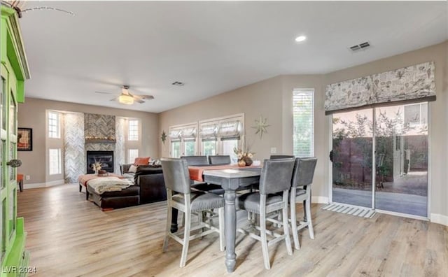 dining room featuring a large fireplace, light hardwood / wood-style floors, and ceiling fan