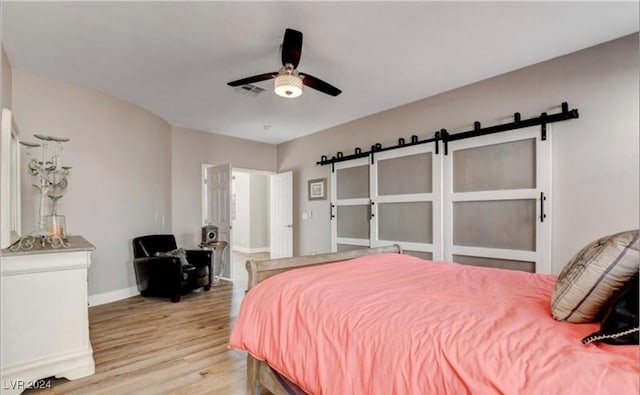 bedroom featuring a barn door, ceiling fan, and light hardwood / wood-style flooring