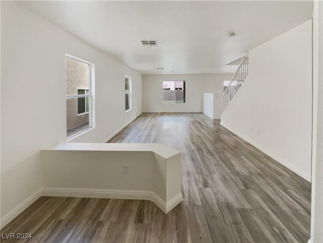 unfurnished living room featuring visible vents, stairs, baseboards, and wood finished floors