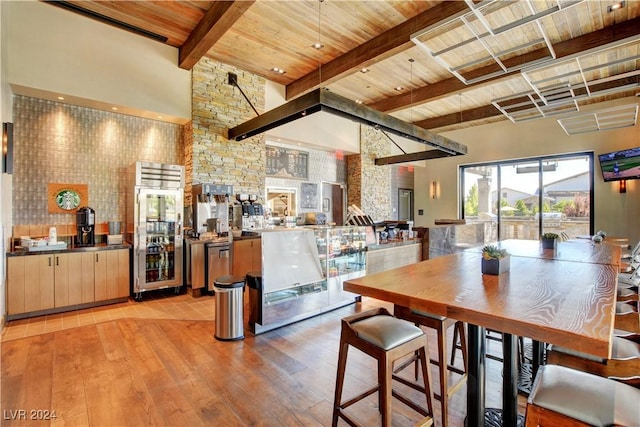 dining space featuring beverage cooler, beam ceiling, light wood-style flooring, a towering ceiling, and wooden ceiling