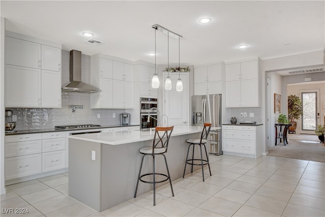 kitchen featuring decorative light fixtures, wall chimney exhaust hood, a center island with sink, a breakfast bar, and stainless steel appliances