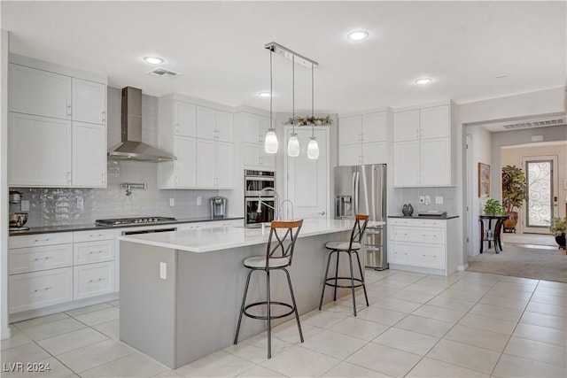 kitchen featuring white cabinetry, stainless steel appliances, a breakfast bar area, wall chimney range hood, and hanging light fixtures