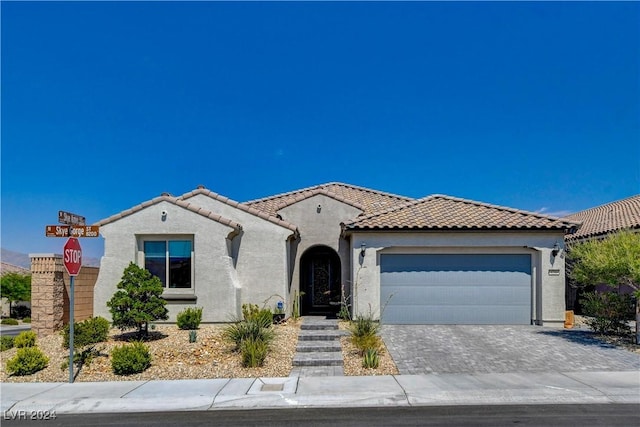 mediterranean / spanish house featuring stucco siding, decorative driveway, an attached garage, and a tile roof