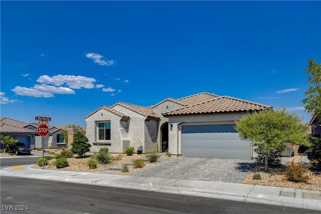 mediterranean / spanish-style house featuring a garage, decorative driveway, stucco siding, and a tiled roof