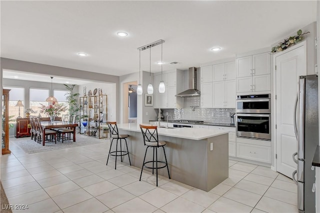 kitchen with tasteful backsplash, white cabinetry, appliances with stainless steel finishes, a breakfast bar area, and wall chimney exhaust hood