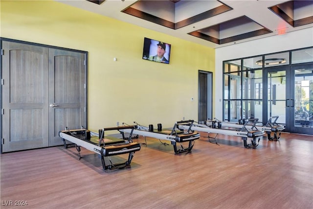 interior space featuring coffered ceiling, a high ceiling, french doors, and wood finished floors