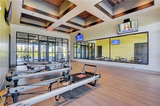 exercise room featuring wood finished floors, coffered ceiling, baseboards, and a towering ceiling