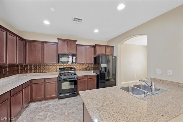 kitchen featuring light stone countertops, decorative backsplash, sink, and black appliances