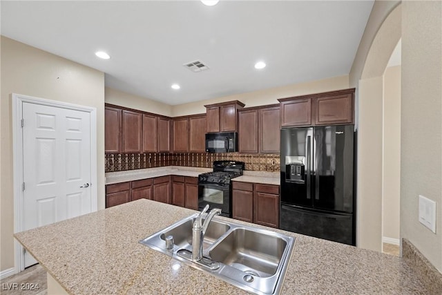 kitchen featuring dark brown cabinetry, light stone countertops, sink, tasteful backsplash, and black appliances