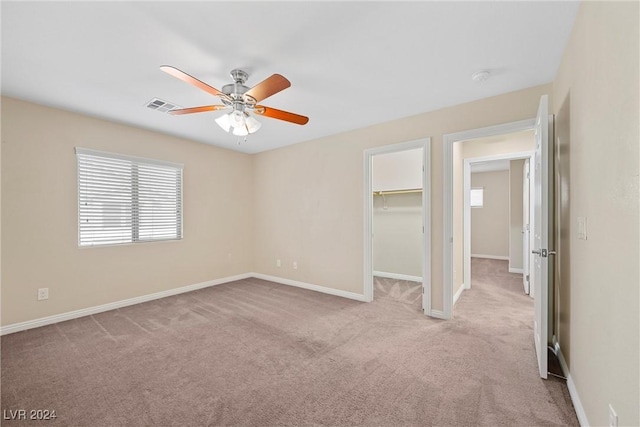 unfurnished bedroom featuring ceiling fan, a spacious closet, light carpet, and a closet