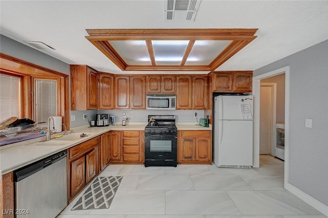 kitchen with washer / dryer, sink, appliances with stainless steel finishes, and a tray ceiling