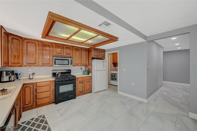 kitchen with washer / dryer, black range with gas cooktop, sink, and white fridge