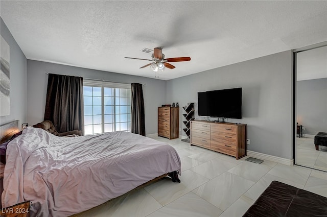 bedroom with a textured ceiling, light tile patterned flooring, and ceiling fan